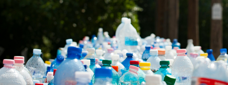 An enormous pile consisting of a variety of empty plastic bottles on the sidewalk next to a hedge.